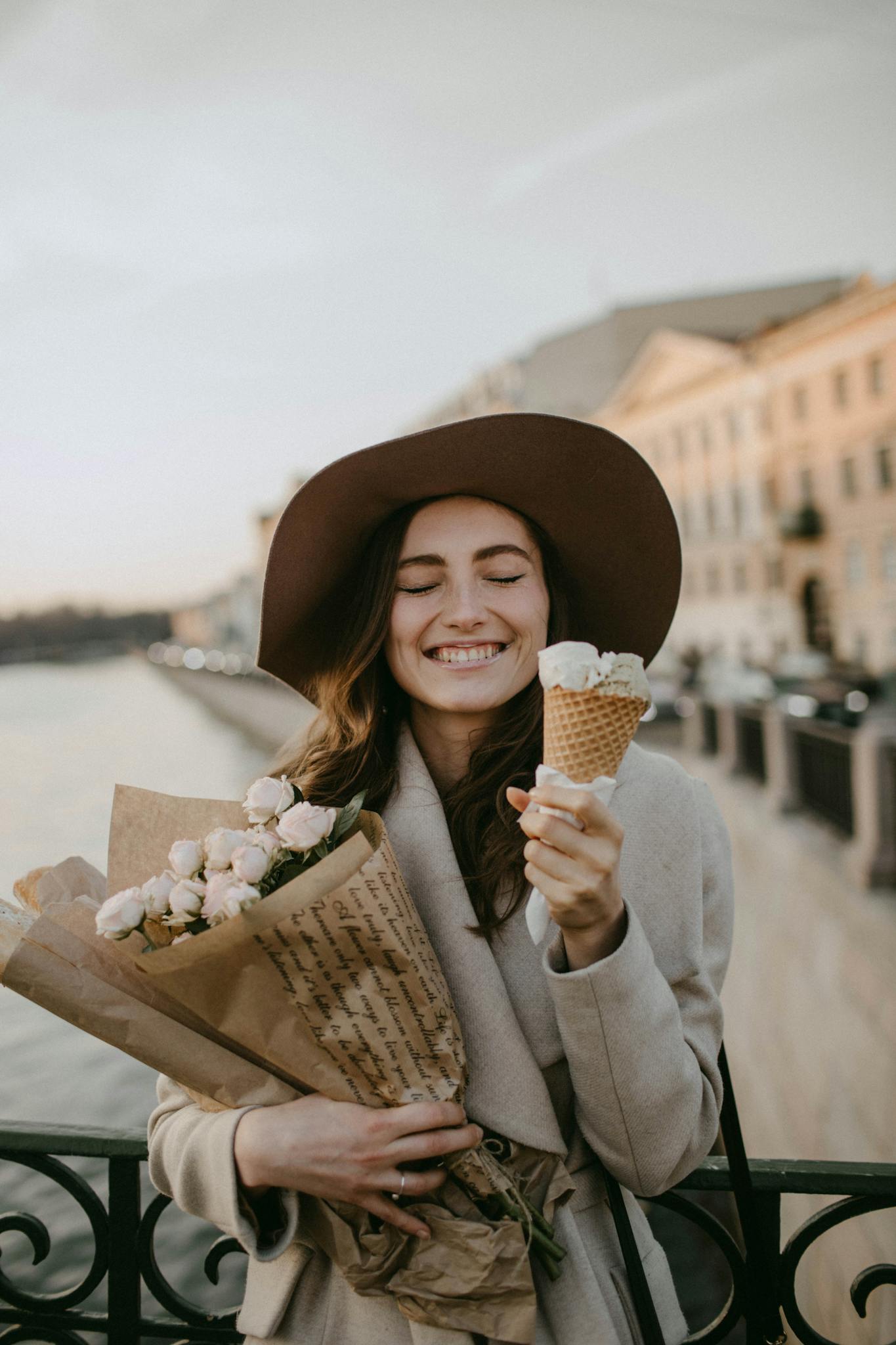 Happy woman with ice cream and flowers by the riverside in a stylish outfit.